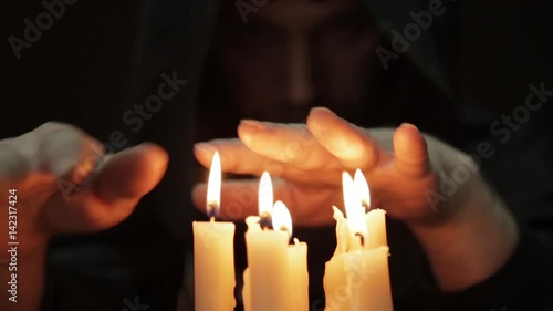 man doing the magic ritual. close-up several candle and old book. necromancer casts spells from thick ancient book by candlelight