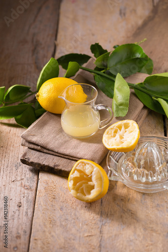 glass bowl of freshly squeezed lemon juice, lemon squeezer and ripe lemons on wooden background