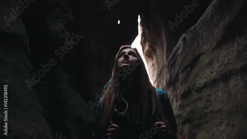 Scared young blonde woman with a backpack walking lost in the dark cave. Dangerous adventure, hiking. Amazing nature.