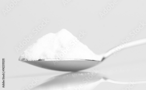 Baking soda in steel spoon isolated on grey background