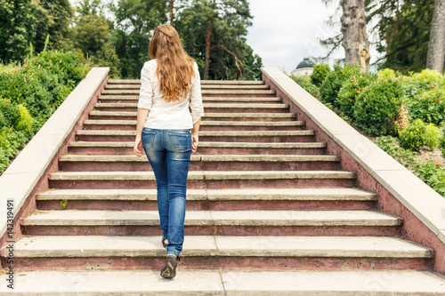 Billede på lærred Rear view of young woman going up the stairs in the park