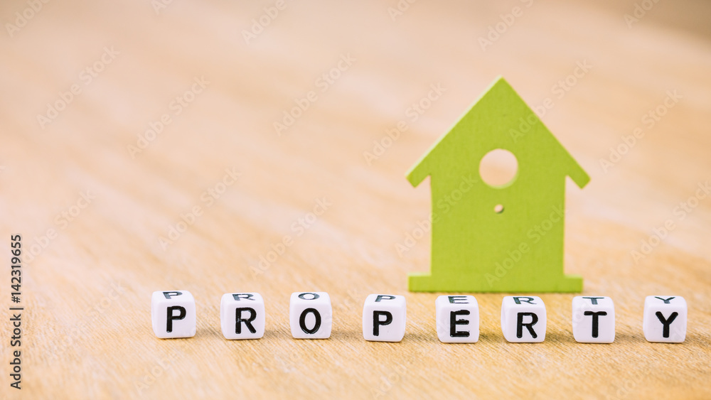 PROPERTY word of cube letters in front of green house symbol on wooden surface. Concept PROPERTY word of cube letters in front of green house symbol on wooden surface. Concept