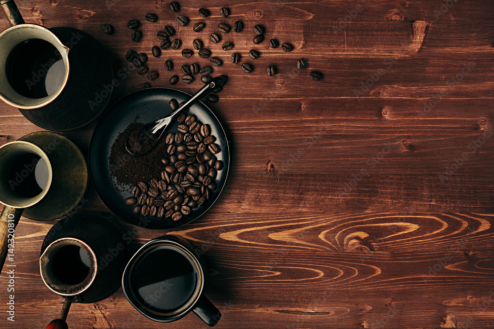 Hot coffee in black cup and turkish pots cezve with beans, saucer with copy space on brown old wooden board background, top view. Rustic style. Hot coffee in black cup and turkish pots cezve with beans, saucer with copy space on brown old wooden board background, top view. Rustic style.