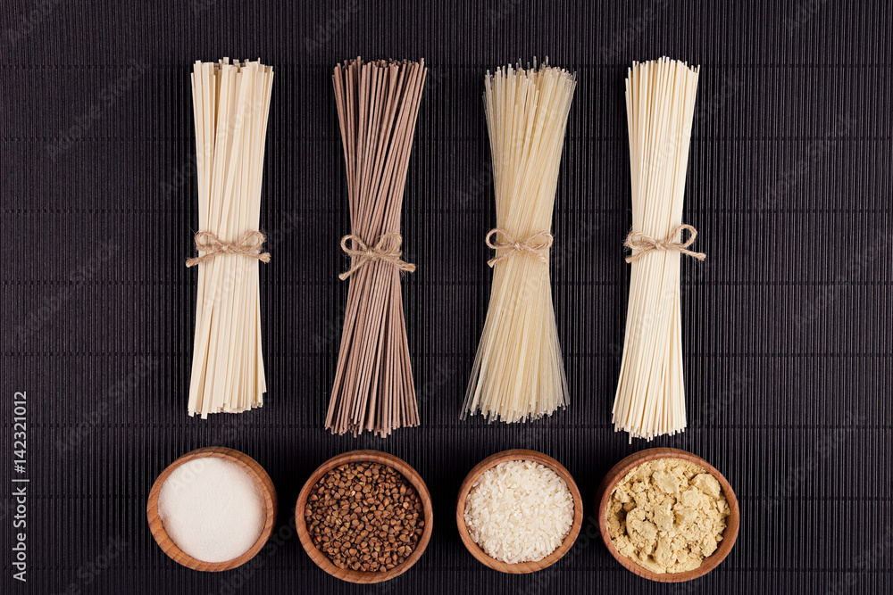 Bundles raw noodles with ingredient in wooden bowls on black striped mat background with copy space, top view. Bundles raw noodles with ingredient in wooden bowls on black striped mat background with copy space, top view.
