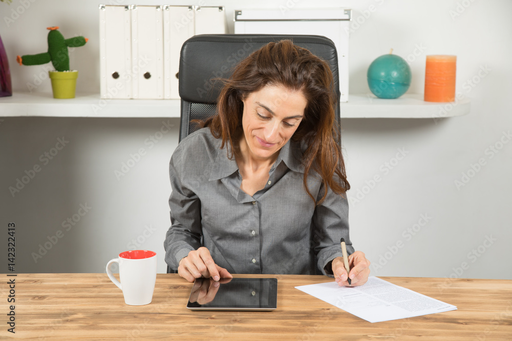 adult brown hair business woman smiling, with grey shirt, sitting using tablet and writing on paper document, on wooden table, in office workplace
adult brown hair business woman smiling, with grey shirt, sitting using tablet and writing on paper document, on wooden table, in office workplace