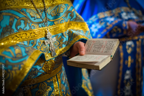 The clergyman reads the Bible, the Bible is in the hands of the priest, the priest is in the Orthodox Christian temple, the Bible in his hands