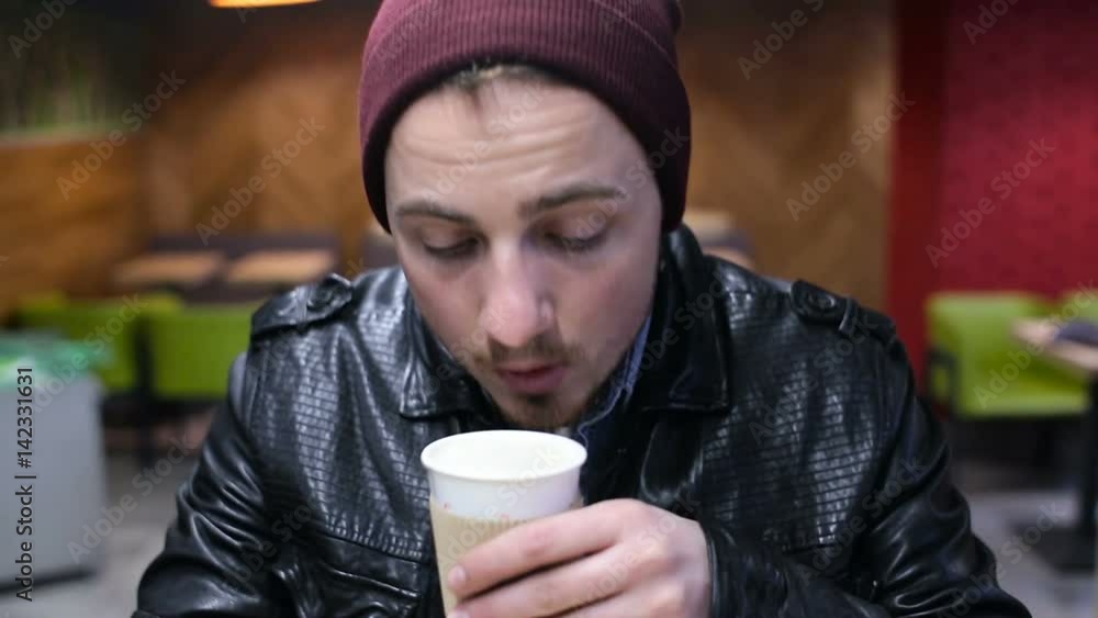 Young hipster guy in a red hat drinks coffee in a cafe Young hipster guy in a red hat drinks coffee in a cafe