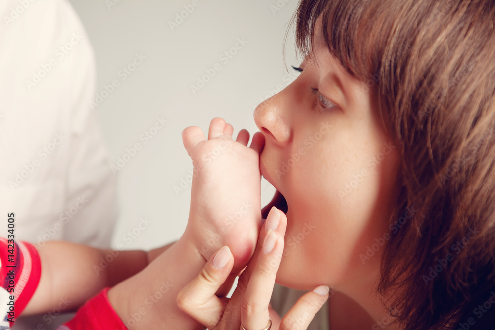 Mom opened her mouth and wants to bite her newborn baby's leg Mom opened her mouth and wants to bite her newborn baby's leg