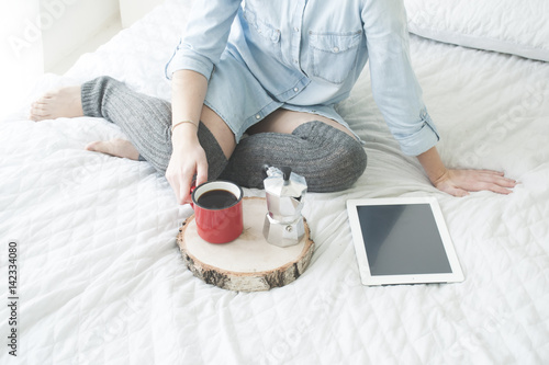 Girl drinking morning coffee on a white bed reading tablet in high stockings photo