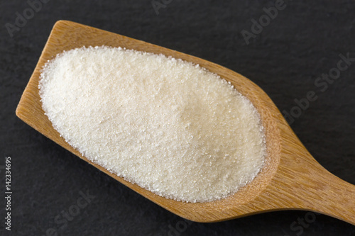 Canvas Print Wooden spoon full of dried white fine powder starch on dark stone background