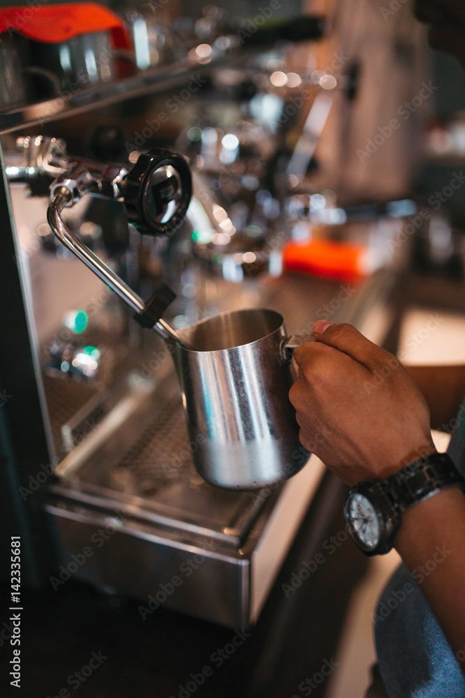 Making fresh espresso or cappuccino coffee in a coffee machine lathering and frothing the milk with hot steam, with the hands of a barista 