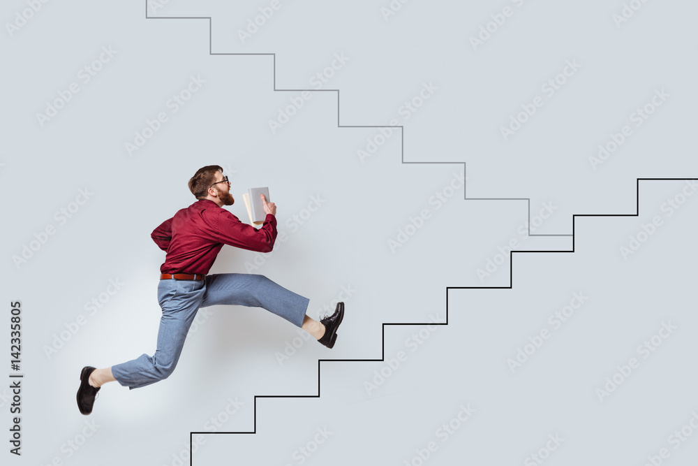 Young bearded man with books running up a drawn stairs