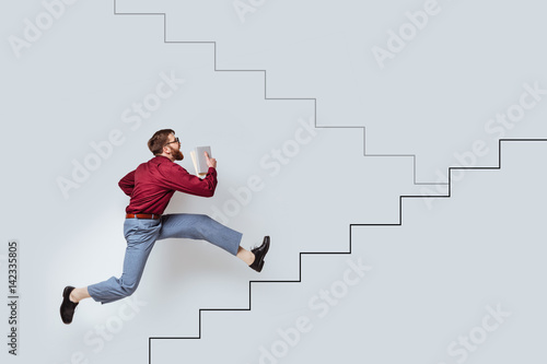 Young bearded man with books running up a drawn stairs photo