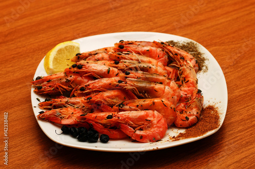 Freshly prepared shrimps lie on a white plate, adorned with spices and lemon. Against the background of a wooden table.