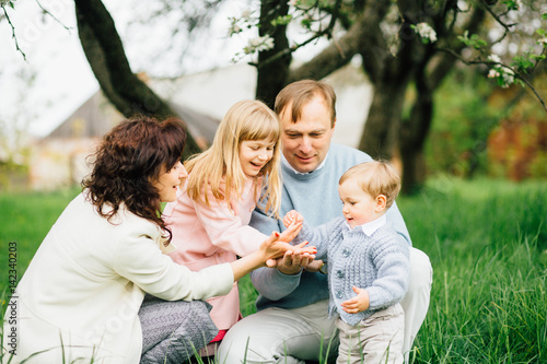 Happy family with two children having fun in the apple-garden and playing with flowers of apple blossom in their hands on a spring day. © Iryna