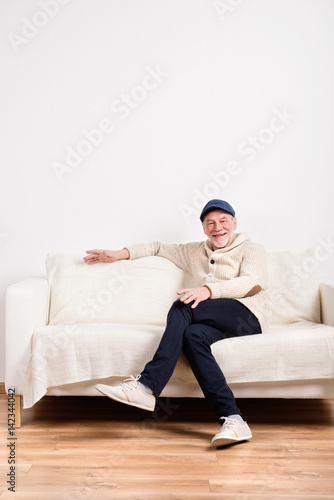 Senior man in beige sweater sitting on sofa, studio shot.