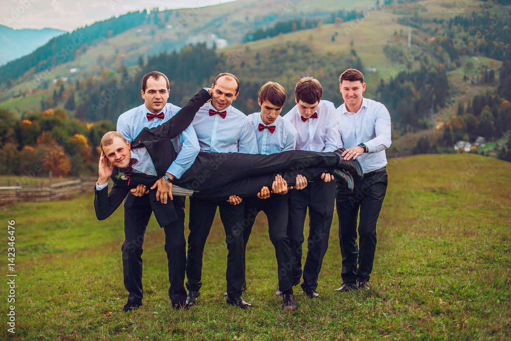 young groom and his funny friends groomsman posing for camera and having fun outdoor near mountains. Group of young men with bow tie. Cheerful friends. friends outdoors. Wedding day.