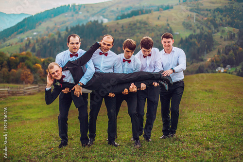 Obraz na płótnie young groom and his funny friends groomsman posing for camera and having fun outdoor near mountains. Group of young men with bow tie. Cheerful friends. friends outdoors. Wedding day. w salonie
