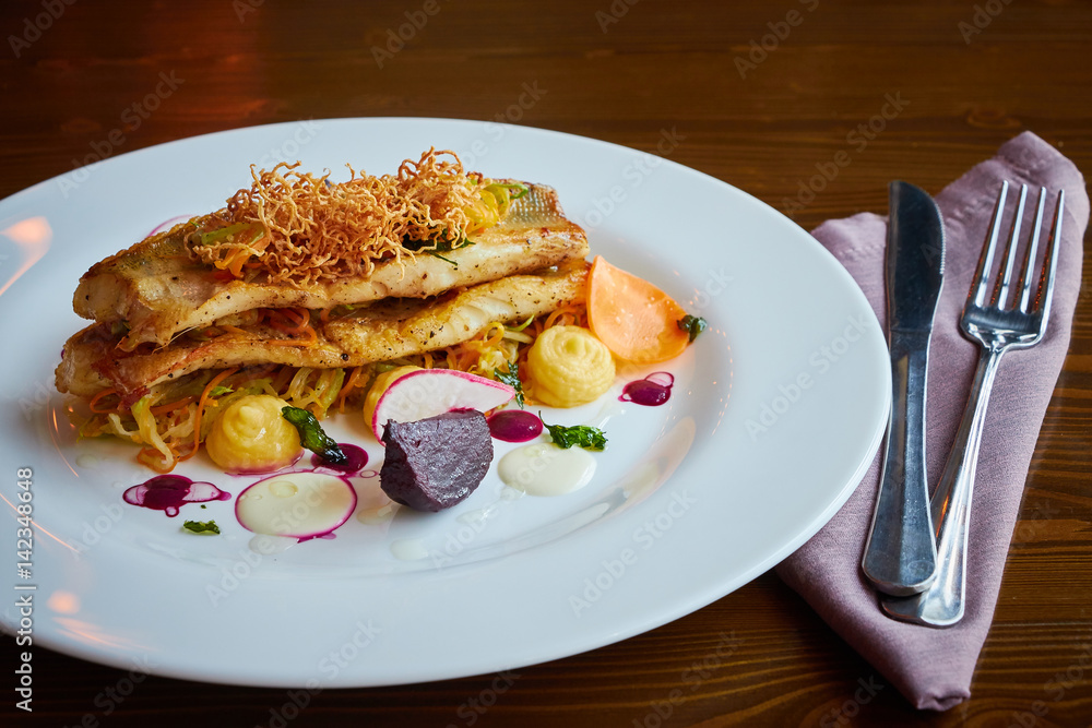 Baked cod fillet with vegetables in restaurant interior Baked cod fillet with vegetables in restaurant interior