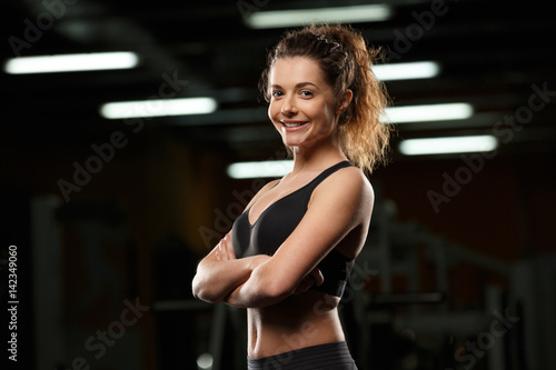 Cheerful sports lady standing in gym with arms crossed