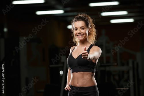 Cheerful sports lady in gym showing thumbs up gesture