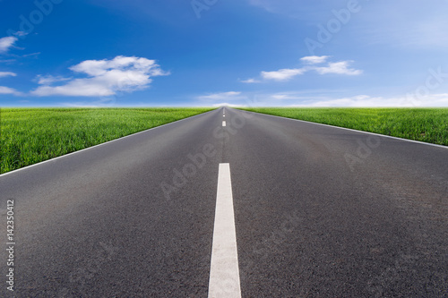 Asphalt road with green field and blue sky
