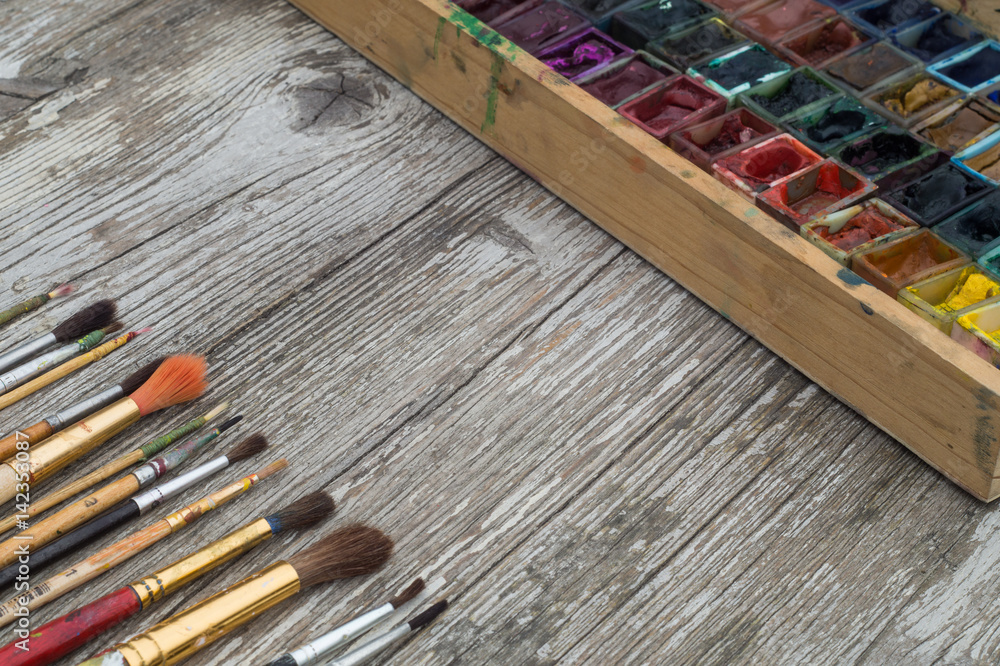 Obraz premium Box with watercolors and brushes on a wooden surface