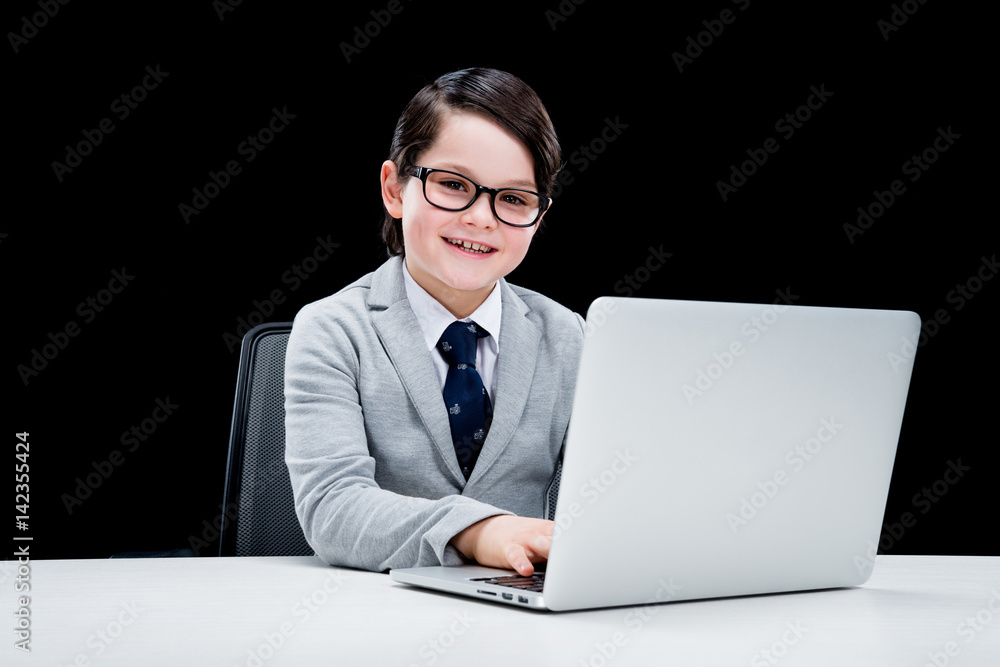 Little boy in formal suit and eyeglasses working with laptop and smiling Little boy in formal suit and eyeglasses working with laptop and smiling