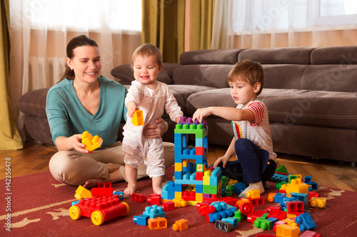 mother and children playing with lots of colorful plastic blocks constructor indoor. The happy family spends time together at home.