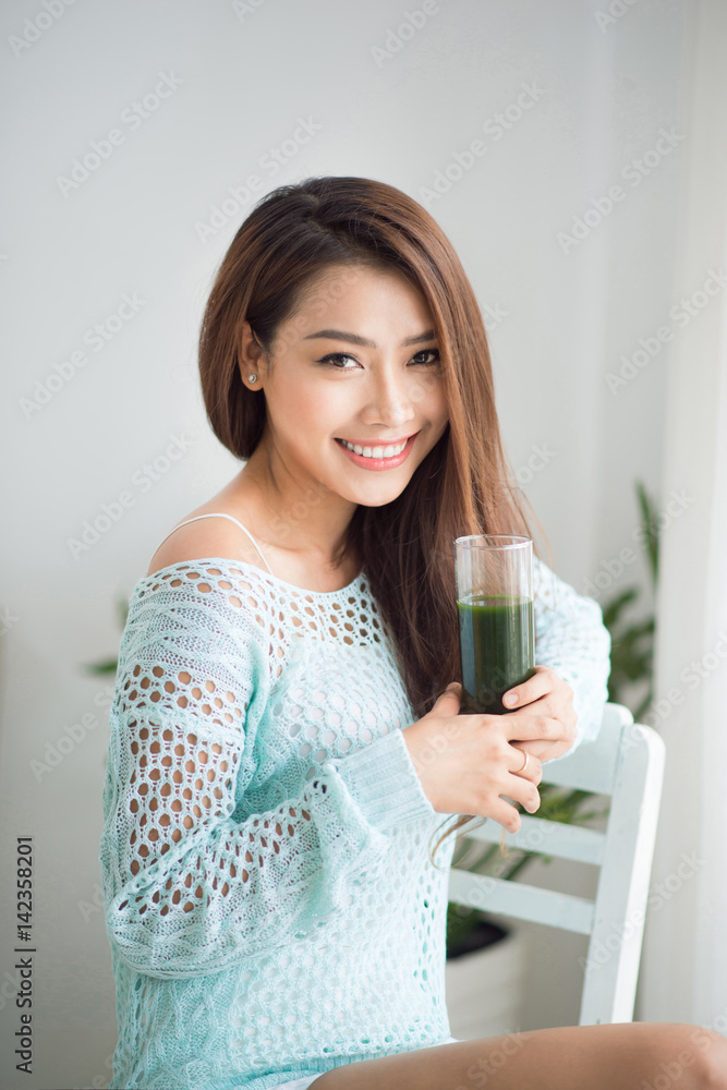 Smiling young asian woman drinking green fresh vegetable juice or smoothie from glass at home Smiling young asian woman drinking green fresh vegetable juice or smoothie from glass at home