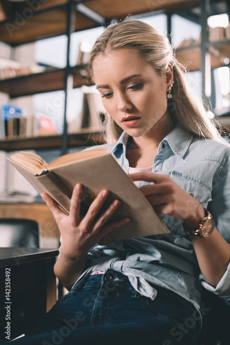 portrait of concentrated woman student reading book in library