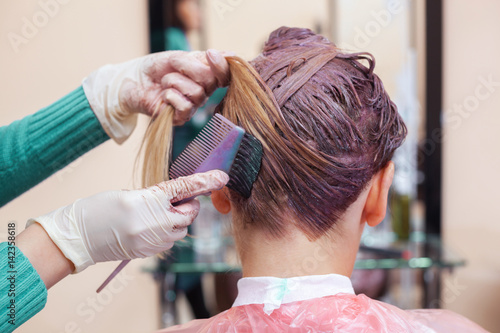 The hairdresser paints the woman's hair in white, apply the paint to her hair in the beauty salon.