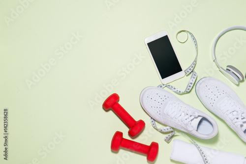 Healthy life concept. Sneakers, headphone, dumbbell and smartphone on pastel color background.