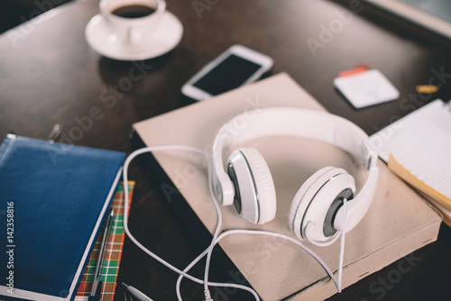 Book, smartphone, cup of coffee, copybooks and headphones on table