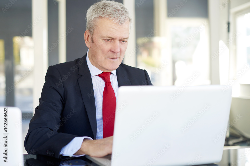 Senior businessman in the office. Shot of a financial managing director sitting in front of laptop and analysing financial data. Senior businessman in the office. Shot of a financial managing director sitting in front of laptop and analysing financial data.