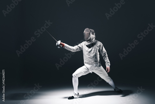 Professional fencer in fencing mask with rapier standing in position on grey © LIGHTFIELD STUDIOS