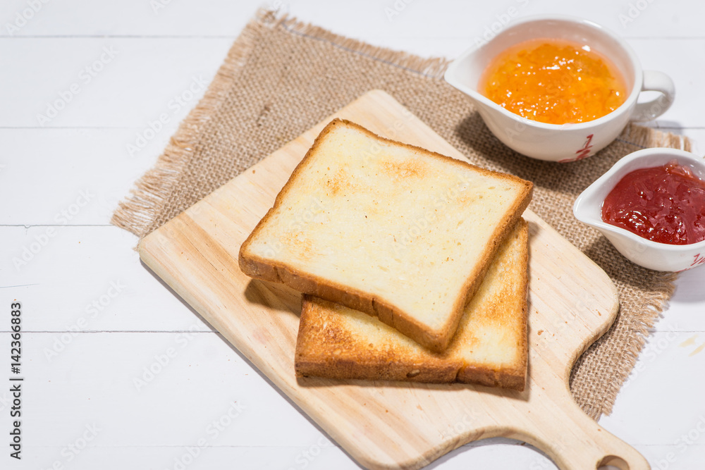 Toast with strawberry and orange jam on a plate on table.