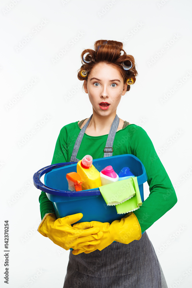 Surprised nice woman holds blue bucket full of cleaning tools Surprised nice woman holds blue bucket full of cleaning tools