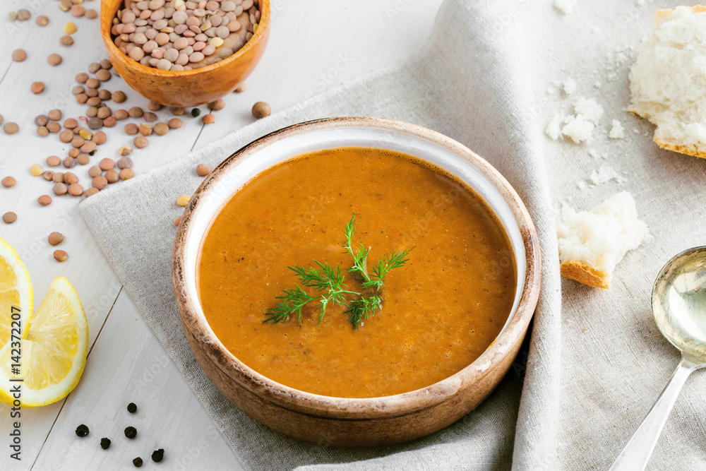 Delicious soup made of lentils in a rustic clay bowl served on a canvas tablecloth. Healthy vegetarian meal on a table. Top view shot. Delicious soup made of lentils in a rustic clay bowl served on a canvas tablecloth. Healthy vegetarian meal on a table. Top view shot.