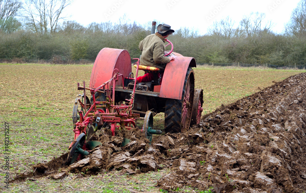 Naklejka premium Vintage red International 1930's tractor ploughing field.