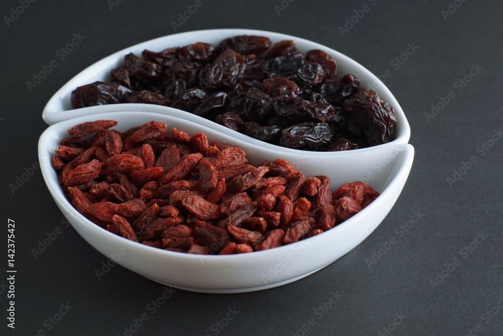 Dried goji berries and raisins in bowls on a dark background, similar to a yin-yang sign Dried goji berries and raisins in bowls on a dark background, similar to a yin-yang sign