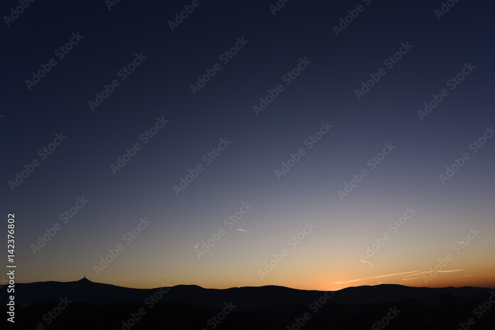 Clear blue sky during sundown behind silhouette of hills.