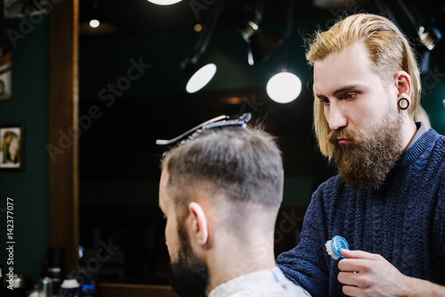 Bearded man sits straight while barder cuts his hair photo