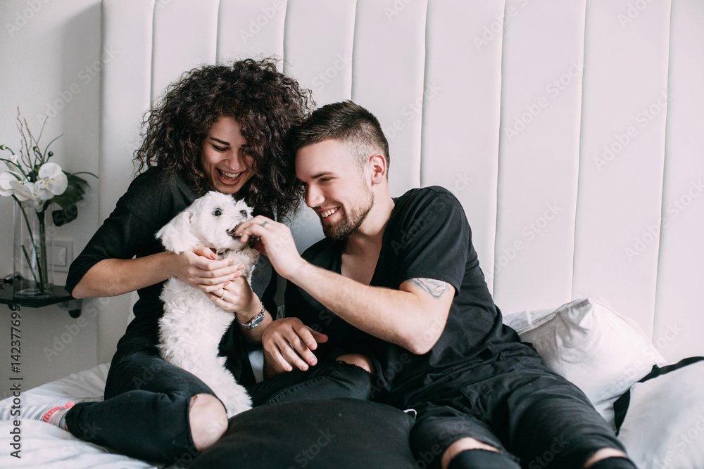 Man and woman in black play with little white dog on bed Man and woman in black play with little white dog on bed