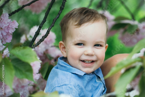 Cute happy boy smiling in mother arms among blossoming flowers