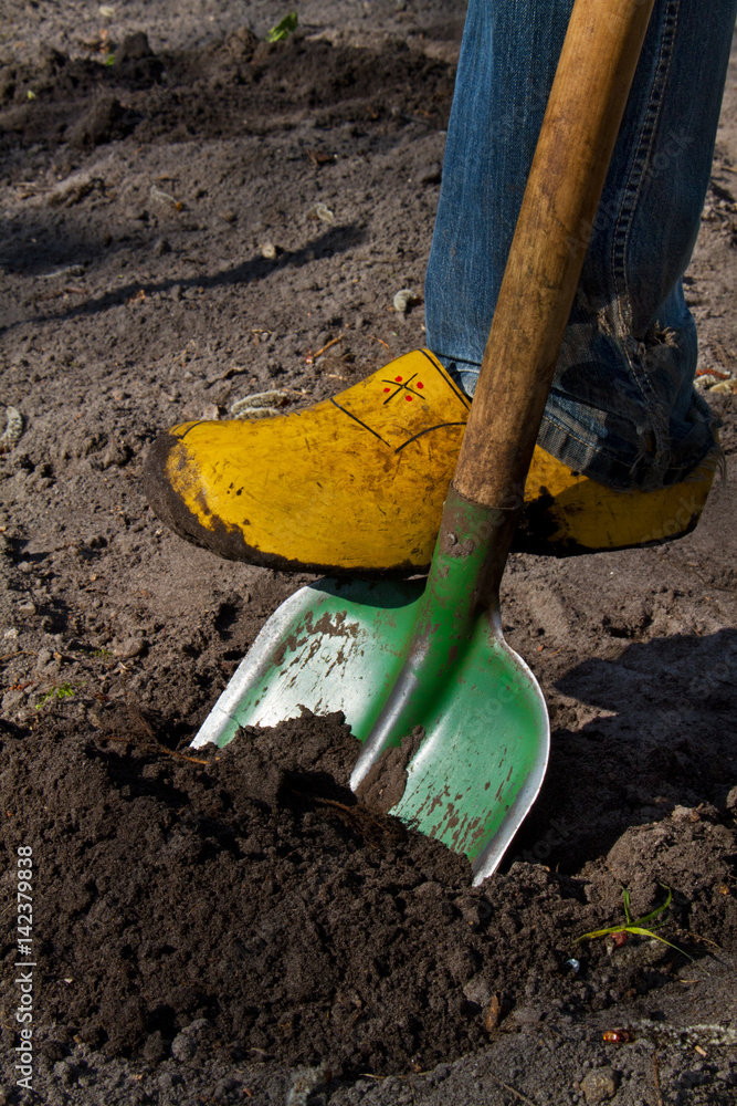Digging the soil with a green spade, wearing clogs Digging the soil with a green spade, wearing clogs