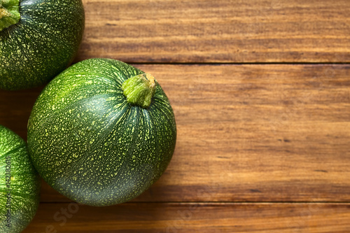 Raw round zucchinis photographed overhead on wood with natural light (Selective Focus, Focus on the top of the zucchinis)