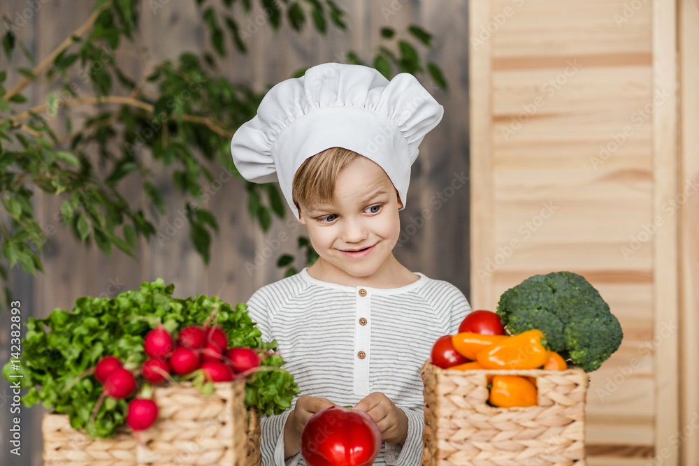 Handsome little kid in chef uniform with vegetables. Cooking in kitchen at home. Vegetarian. Healthy food Handsome little kid in chef uniform with vegetables. Cooking in kitchen at home. Vegetarian. Healthy food