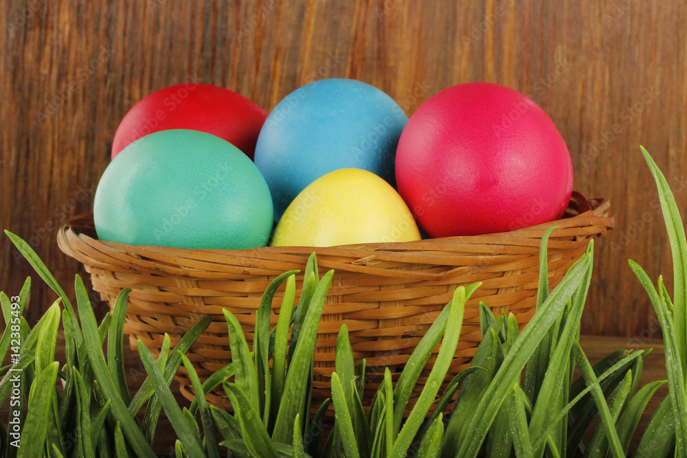 Naklejka premium coloured eggs in grass on wooden background
