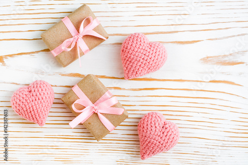 Пара упакованных подарков с розовой лентой и вязанные сердца на белом деревянном фоне
